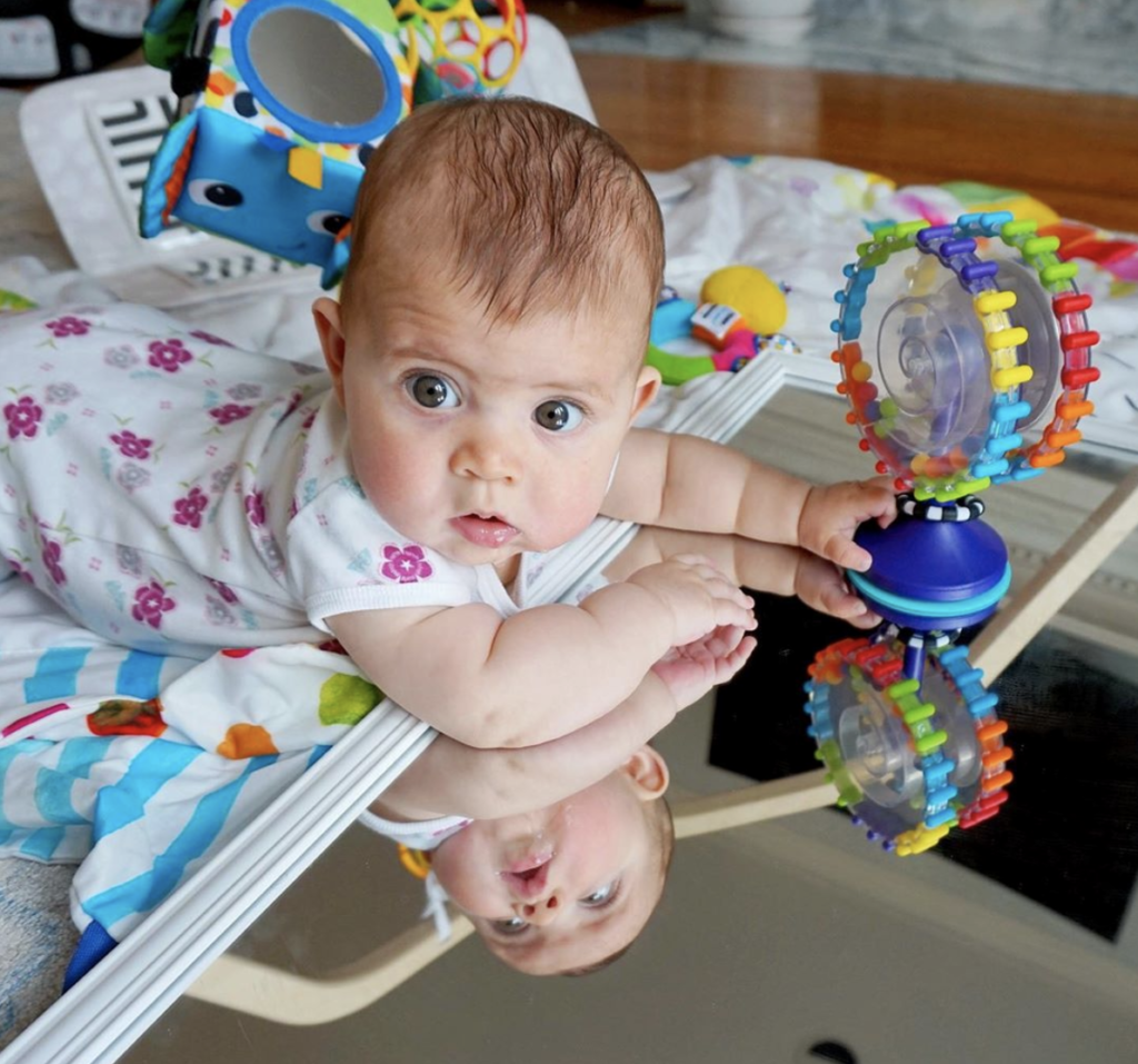 Baby playing stomach playing on a mirror with toys
