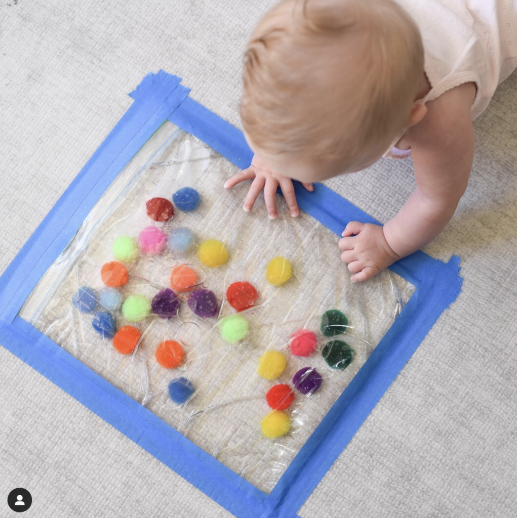 Baby playing tummy with a sensory bag on floor
