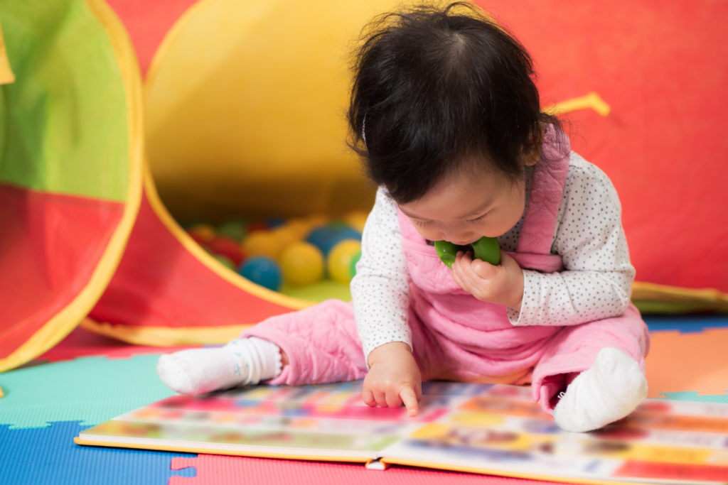 An infant reading a colorful book on the floor.